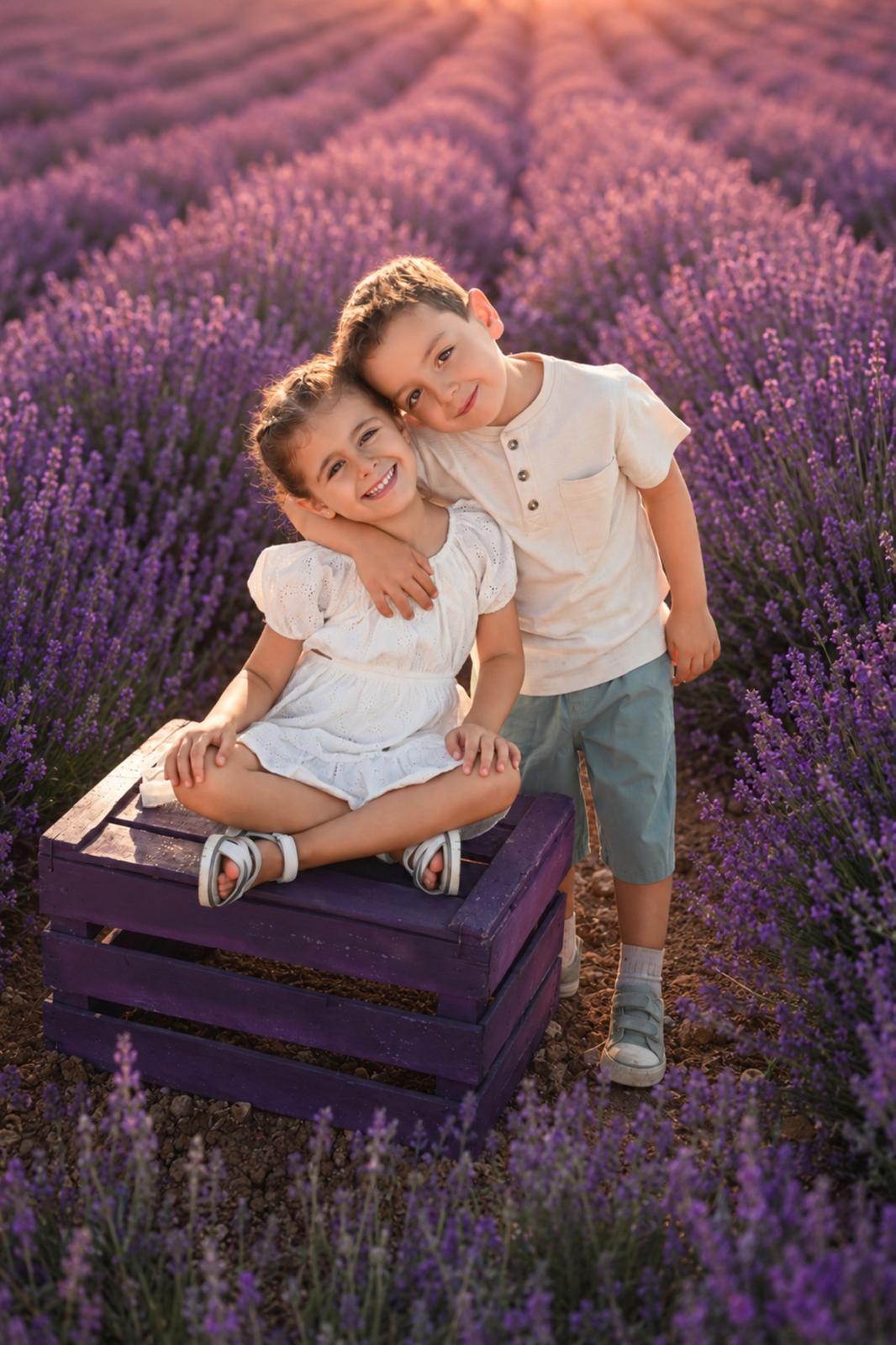 Dos hermanos abrazados sobre una caja morada en un campo de lavanda al atardecer
